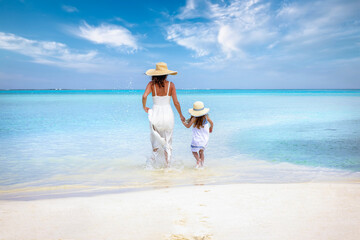 A mother and daughter in white dresses running into the turquoise sea of the Indian Ocean, Maldives, during their beach holidays