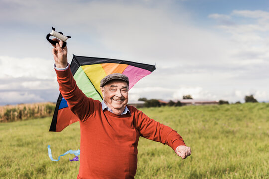 Happy senior man flying multi colored kite at field