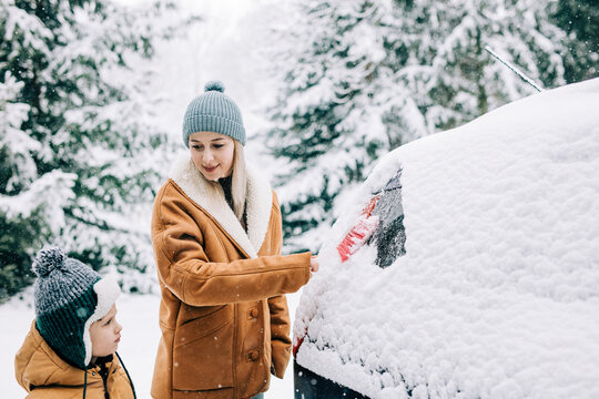 Woman standing near son and scraping snow from car