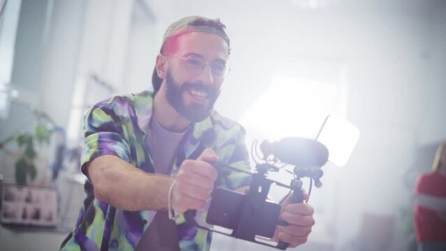 Portrait of Enthusiastic Male Videographer Filming a Project Using Smartphone Rig Equipment in a Bright Studio. Professional Online Content Maker Directing his Actors While Filming Them