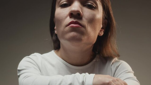 Tilt up slowmo portrait of young serious Caucasian woman with dwarfism sitting on office chair and looking down at camera on gradient grey background