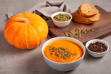 Pumpkin soup with seeds, spices, pepper and bread on a gray background. The concept of healthy vegetable soups. Concept of healthy eating or vegetarian food. Healthy seasonal autumn cuisine