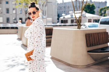 Young beautiful confident woman in trendy summer white costume clothes. Sexy carefree model posing in the street at sunset. Positive brunette female. Cheerful and happy. In sunglasses, red lips