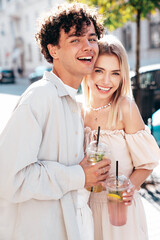 Young smiling beautiful woman and her handsome boyfriend in casual summer clothes. Happy cheerful family. Female having fun. Couple posing in street. Holding and drinking cocktail drink in plastic cup