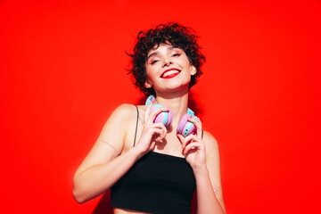 Young beautiful smiling female in trendy summer tank top. Carefree woman posing near red wall in...