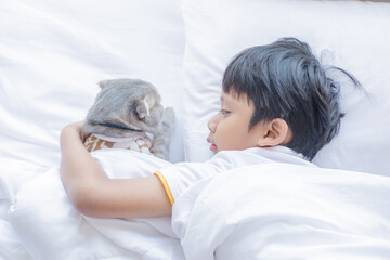 A young Asian boy kid is sleeping with his cat pet. Child hug a little kitten in bed.