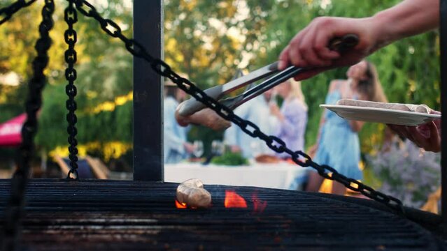 An unrecognizable man grills food during a family summer garden party on a warm evening. Close-up of aromatic and delicious food at an outdoor party.