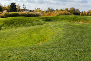 Slightly hilly lawn covered with trimmed green grass at autumn