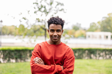 portrait of young adult african american guy with arms crossed and a red sweater looking at camera...