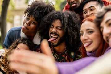 detail close up on young adult African American man with tongue gesturing joking with his group of friends while taking a selfie