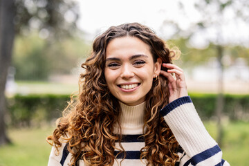 portrait of young adult woman looking at camera and smiling putting her hair behind her ear