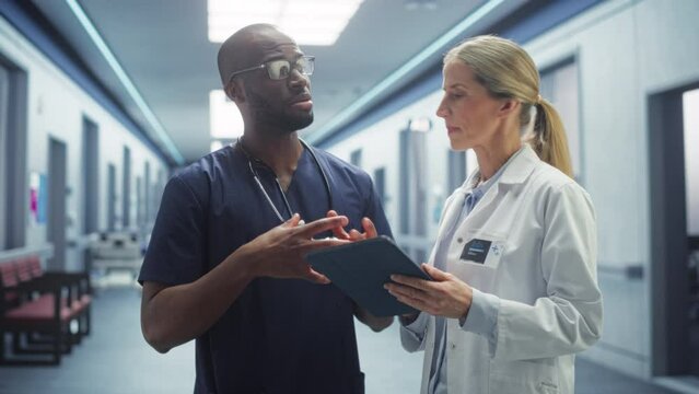 Hospital Ward: Female Doctor Talks With Professional Black Head Nurse or Surgeon, They Use Digital tablet Computer. Diverse Team of Health Care Specialists Discussing Test Result in Modern Clinic