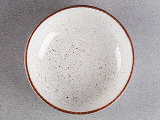White empty deep clay plate with a spoon on a gray background.
