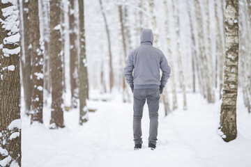 Young adult man walking on fresh white snow at birch tree forest in beautiful cold winter day....