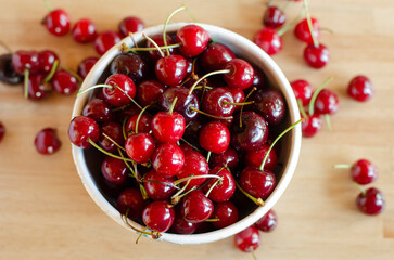 freshly picked bright sweet red cherries in white ceramic bowl on wooden table