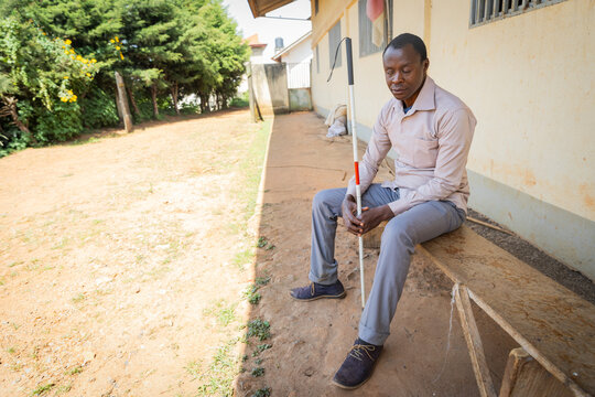 Blind man sitting on a wooden bench holding his white cane.