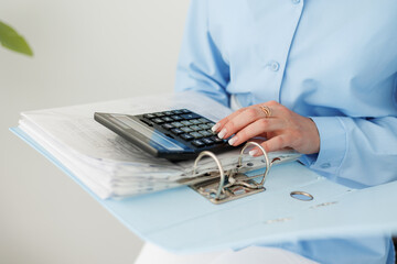 Cropped photo of female accountant in blue shirt calculates on calculator costs, counts money,...