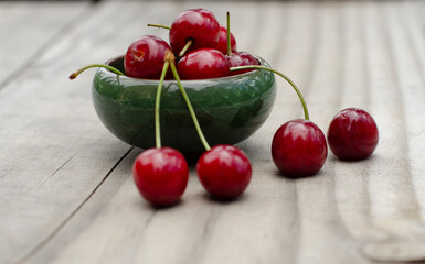 Fresh and sweet freshly harvested cherries in green bowl on wooden deck