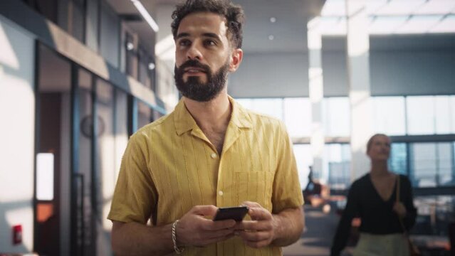 Portrait of Successful Latin Businessman Walking In Office Building Using Smartphone. Male Digital Entrepreneur uses Mobile Phone e-Commerce App for Stock Market Investment, Smiling Happily