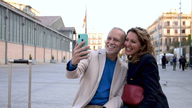 Happy mid adult tourist couple travelling together taking a selfie with her luggage. Affectionate senior husband and wife taking a picture during a weekend romantic trip in european city
