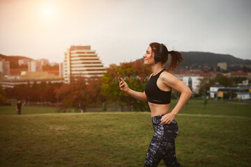 Athletic young woman with hair in a ponytail in leggings and a top with headphones is jogging on...