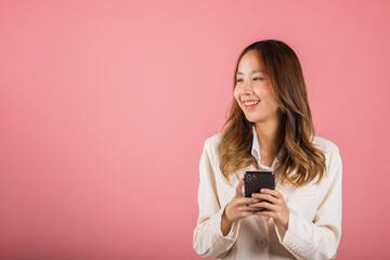 Happy Asian portrait beautiful cute young woman teen smiling excited hold smart mobile phone studio...