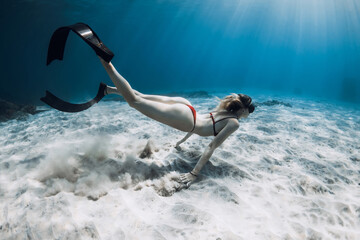 Woman free diver swims underwater over sandy sea bottom. Freediving in tropical blue ocean