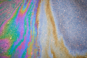Multi-colored poisonous spots of spilled gasoline on wet pavement during rain.