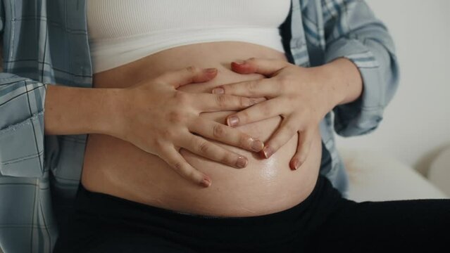Woman massaging pregnant tummy by hands. Female doing massage with oil on belly during pregnancy to avoid appearance of stretch marks on skin. Expecting baby, healthy self cafe, bodycare concept.