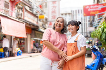 Happy Asian family grandmother and grandchild girl walking and shopping together at street market....