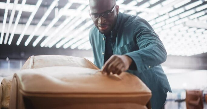 Portrait of a Handsome Automotive Designer Developing a 3D Clay Model of a New Production Car. Professional Black Man Using a Spatula to Smooth Out and Trim the Surface of a Prototype Concept Car