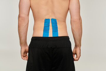 cropped view of man in black sport pants with kinesiological tapes on his back on gray backdrop