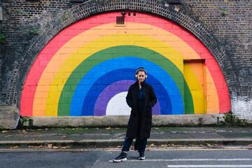 Woman wearing wireless headphones and standing in front of rainbow wall