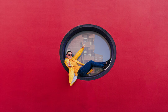 Woman in yellow rain coat sitting in porthole making victory sign