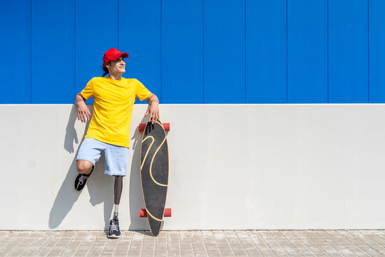 Smiling young man with disability standing near skateboard on sunny day