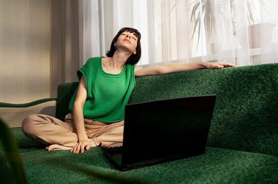 Female freelancer with eyes closed sitting on sofa near laptop at home
