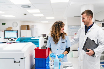 Two healthcare workers engage in cheerful discussion amidst blood analysis machinery in a...
