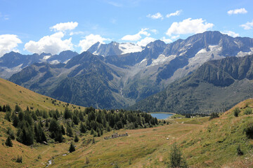 Landscape with fields, lake and mountains in the Italian Alps, under a brilliant sunny an cluody sky