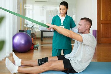 Mature man with injured knee doing exercise with resistant band in rehabilitation center
