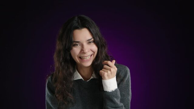 The girl is laughing hysterically, looking into the camera, unable to stop her laughter. She is on a purple background. High quality 4k footage