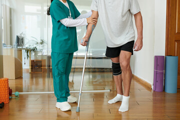Obraz premium Cropped image of patient of rehabilitation center walking with crutch under control of medical nurse