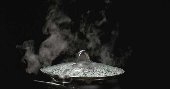 Boiling water in a pan. Steam rising from the pot while cooking on black background