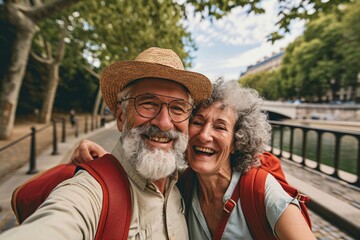 Joyful senior couple with a straw hat and backpacks taking a smiling selfie on a sunny day outdoors