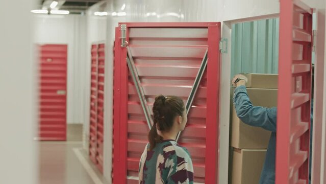 Young family couple leaving cardboard boxes for safekeeping in self storage and closing doors of unit