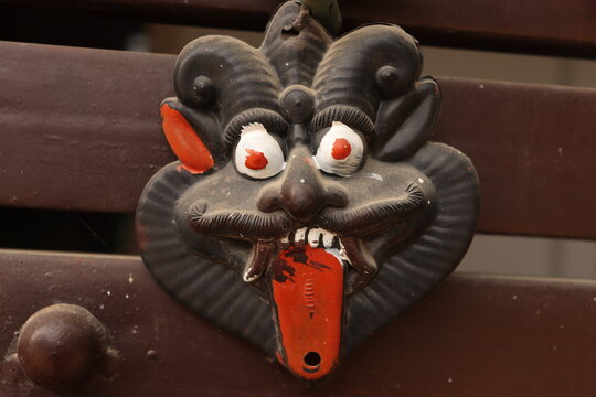 An Indian Black evil eye nazar battu mask with nimbu mirchi or lemon and chilly sign attached by string on iron gate, closeup