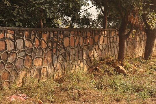 A wall made up of zin stones and brown vintage stone creating a indian mexican style stone wall design under sunlight, in garden
