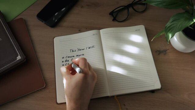 A hand writes a plan for the next year with a black felt-tip pen in a notebook. The concept of planning, motivation and setting goals for the next year. This year I will