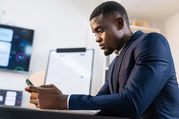 African man using smart phone while sitting at work place. Businessman sitting in modern office.
