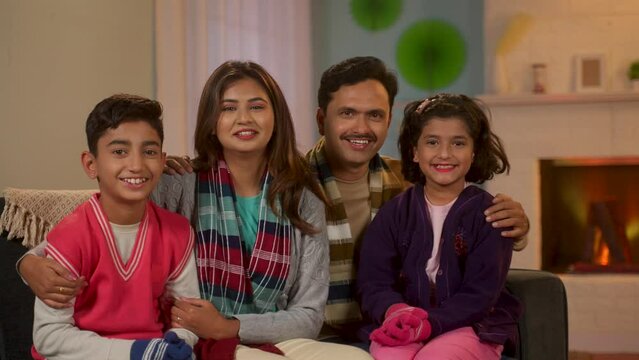Indian happy family in winter wear looking camera at home while spending time together - concept of family bonding, holiday gathering and leisure lifestyles