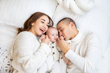 Fototapeta na wymiar Happy family with one baby spending time at home. Parents playing with their baby on bed.